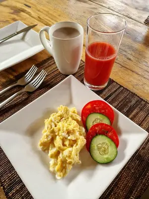 a plate of eggs and cucumbers and a glass of juice at Dolly Farm & River Camp, Luxury Tents in Usa River