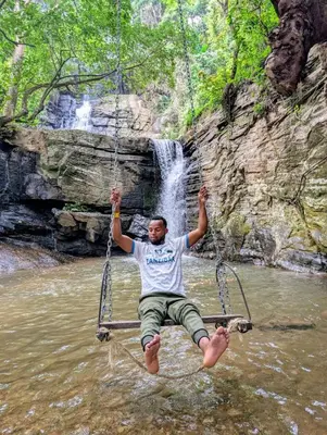 a man on a swing in the water in front of a waterfall at Meleji House in Arusha
