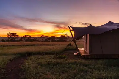 a tent in a field with a sunset in the background at Anantya Serengeti in Serengeti