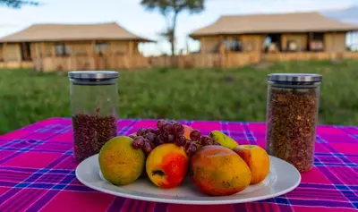 a plate of fruit on a table with two jars of food at Serengeti Malaika Luxury Camp in Serengeti National Park