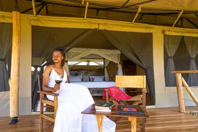 a woman in a white dress standing in front of a bed at Serengeti Malaika Luxury Camp in Serengeti National Park