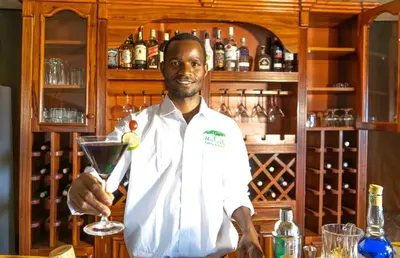 a man standing behind a bar holding a drink at Serengeti Malaika Luxury Camp in Serengeti National Park