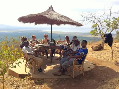 a group of people sitting at a table with an umbrella at Panorama Safari Camp in Mto wa Mbu