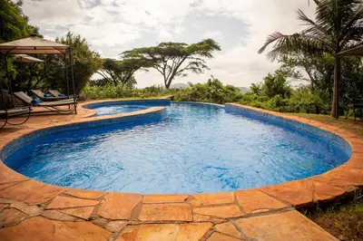 a large swimming pool with a stone walkway around it at Rhotia Valley Tented camp in Karatu