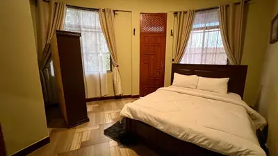 a bedroom with a bed with white sheets and two windows at Skill forest lodge in Arusha
