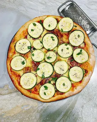 a pizza with cucumbers on it sitting on a table at The Kilimanjaro Villa in Moshi
