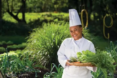 a woman in a chefs hat holding a basket of vegetables at Dik Dik Hotel in Arusha