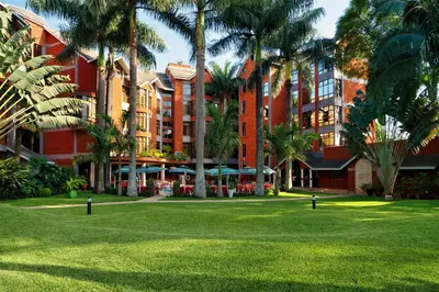 a large red building with palm trees in a park at Kibo Palace Hotel Arusha in Arusha
