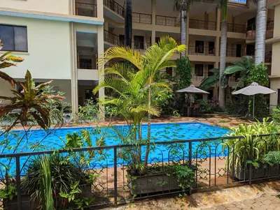 a swimming pool in front of a building with palm trees at Parkview Inn in Moshi