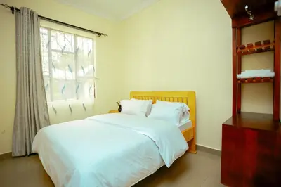a bedroom with a bed with white sheets and a window at BCB Homes in Moshi