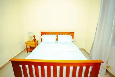 a bedroom with a wooden bed with white sheets at BCB Homes in Moshi