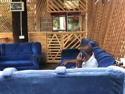 a man sitting on a couch talking on a cell phone at Kilibase Hotel in Moshi