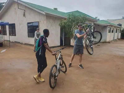two men are holding their bikes in front of a building at Kilibase Hotel in Moshi