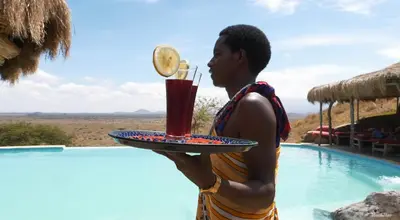 a man holding a drink on a tray next to a pool at Original Maasai Lodge – Africa Amini Life in Ngare Nanyuki