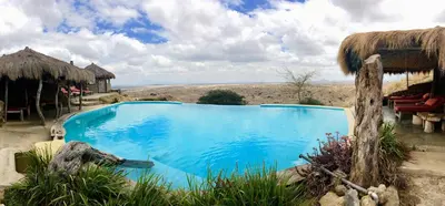 a large blue swimming pool in a field with a hut at Original Maasai Lodge – Africa Amini Life in Ngare Nanyuki
