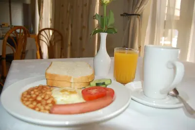 a plate of breakfast food with eggs bread beans and a glass of orange juice at New Safari Hotel in Arusha
