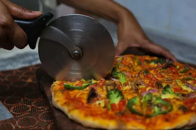 a person cutting a pizza with a pizza cutter at New Safari Hotel in Arusha
