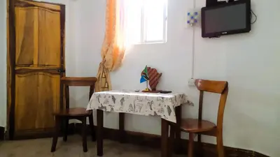 a table with two chairs and a television and a table with a tablecloth at Home Feeling Neneu Lodge in Moshi