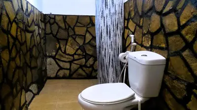 a bathroom with a toilet and a stone wall at Home Feeling Neneu Lodge in Moshi