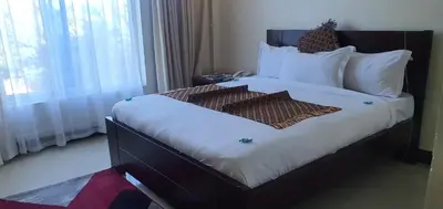 a bedroom with a bed with white pillows and a window at Corridor Springs Hotel in Arusha