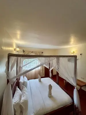 a bedroom with a canopy bed with white sheets and pillows at Patamu Restaurants Lodge & Safaris in Karatu