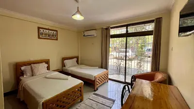 a small room with two beds and a window at Runako Hostel in Arusha