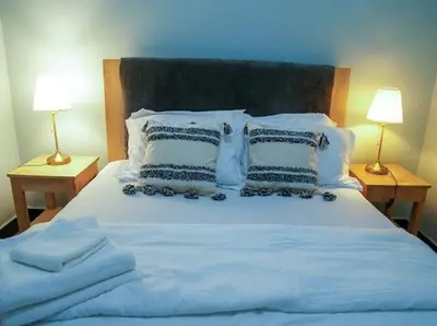 a bed with white sheets and pillows with two lamps at ILBORU HAVEN HOMEs in Arusha