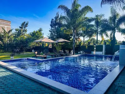 a pool with chairs and umbrellas in a yard with palm trees at The New Njiro Legacy in Arusha