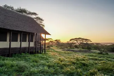 a hut in a field with the sunset in the background at Lake Ndutu Luxury Tented Lodge in Sinoni