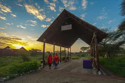 two people walking through a pavilion with the sunset in the background at Lake Ndutu Luxury Tented Lodge in Sinoni