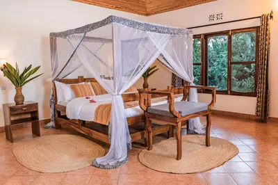 a bedroom with a canopy bed and a chair at KUDU LODGE & CAMPSITE in Karatu