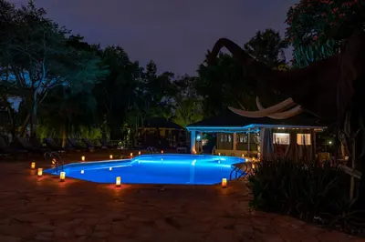 a blue swimming pool with lights in a yard at night at KUDU LODGE & CAMPSITE in Karatu