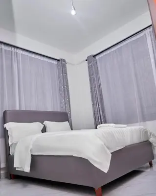 a bedroom with a bed with white sheets and windows at Diamond Apartments in Arusha