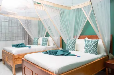two beds in a room with blue curtains at Kigongoni Gazella Hotel in Mto wa Mbu
