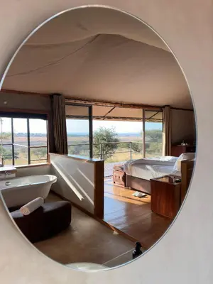a circular mirror in a bedroom with a bed and a tub at Salinero Serengeti in Ututwa