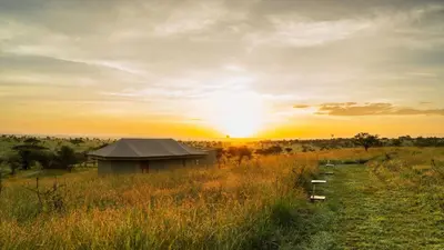 a building in a field with the sunset in the background at Salinero Serengeti in Ututwa