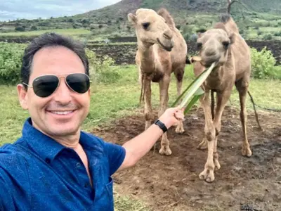 a man holding a stick in front of three camels at Eco Farm in Karatu