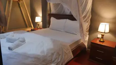 a bedroom with a white bed with two lamps and two bedsskirts at Jangwani River View Suits in Mto wa Mbu