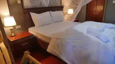 a bedroom with a large white bed and a night stand at Jangwani River View Suits in Mto wa Mbu