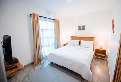 a bedroom with a white bed and a large window at Katiti Lodge in Arusha