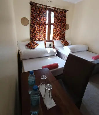 a room with three beds and a table and a window at Hansat Homestay Residence in Arusha