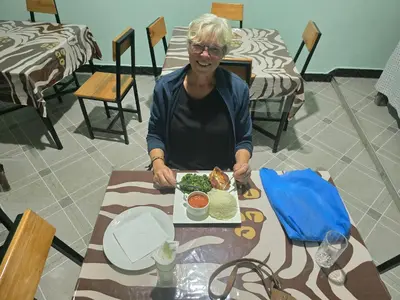 a woman sitting at a table with a plate of food at Lasts minute lodge in Boma la Ngombe