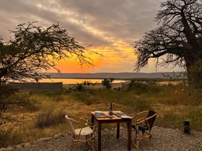 a table and two chairs with the sunset in the background at Suricata Boma Lodge in Mto wa Mbu