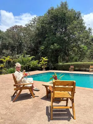 a woman sitting at a table next to a pool at Kilimanjaro Lodge Cabins in Moshi