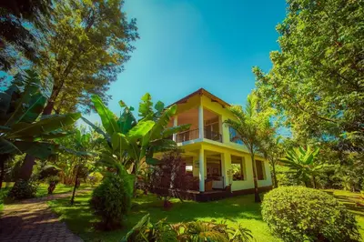 a yellow house with a porch and trees at House of West Kili in Bondeni Boloti