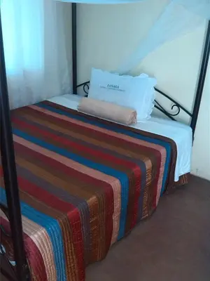 a bed with a striped blanket and a pillow on it at Fanaka Safaris Campsite & Lodges in Mto wa Mbu