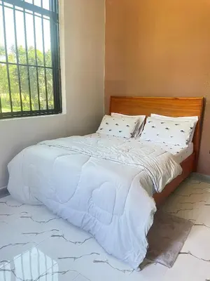 a bedroom with a bed with white sheets and a window at Stay with Rodjazz in Usa River