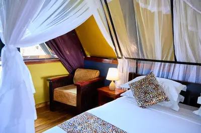 a bedroom with a bed and a chair and a window at Shamba Lodge Cabin X in Arusha