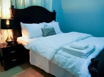 a bed with white sheets and pillows next to a lamp at ILBORU HAVEN HOMEs in Arusha