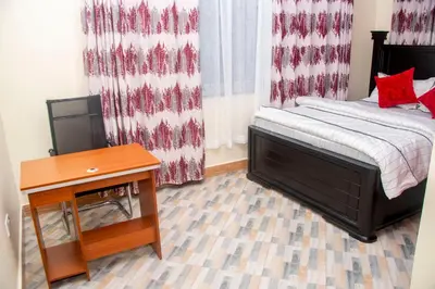 a bedroom with a bed and a table and curtains at VvEK B&B APARTMENT in Arusha